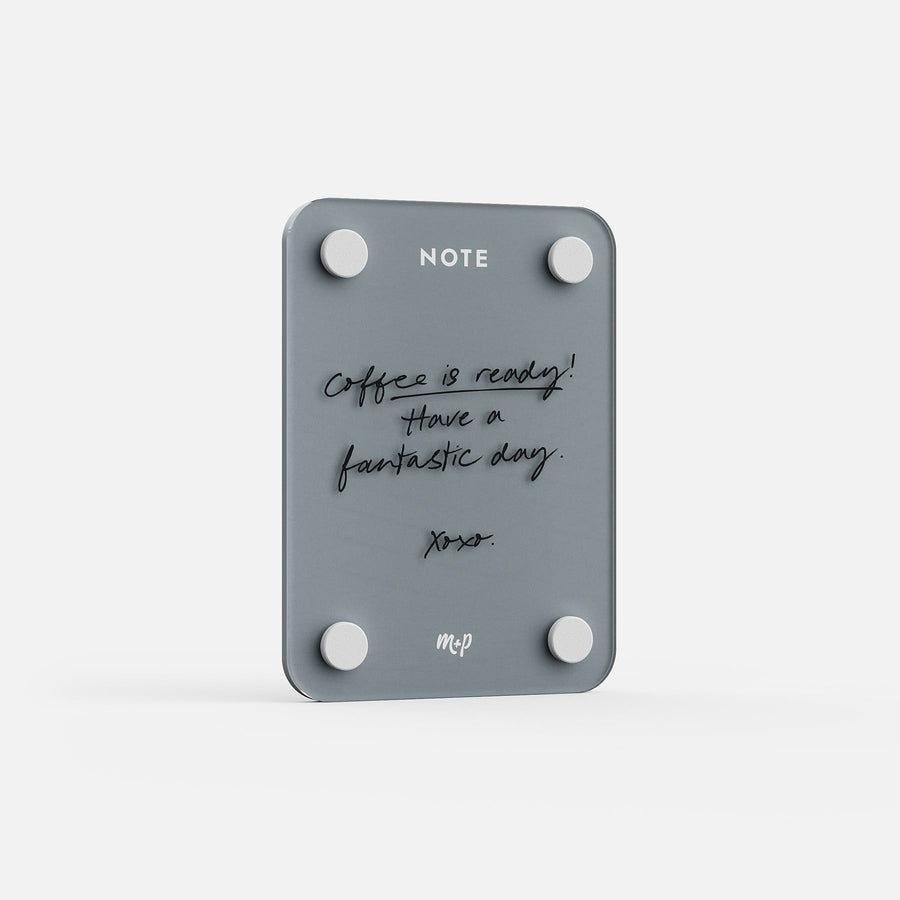The Little Note 35 is a gray magnetic board with four round magnets and handwritten text, “Coffee is ready! Have a fantastic day. xoxo.” NOTE is printed at the top—an ideal modern reminder for your space.