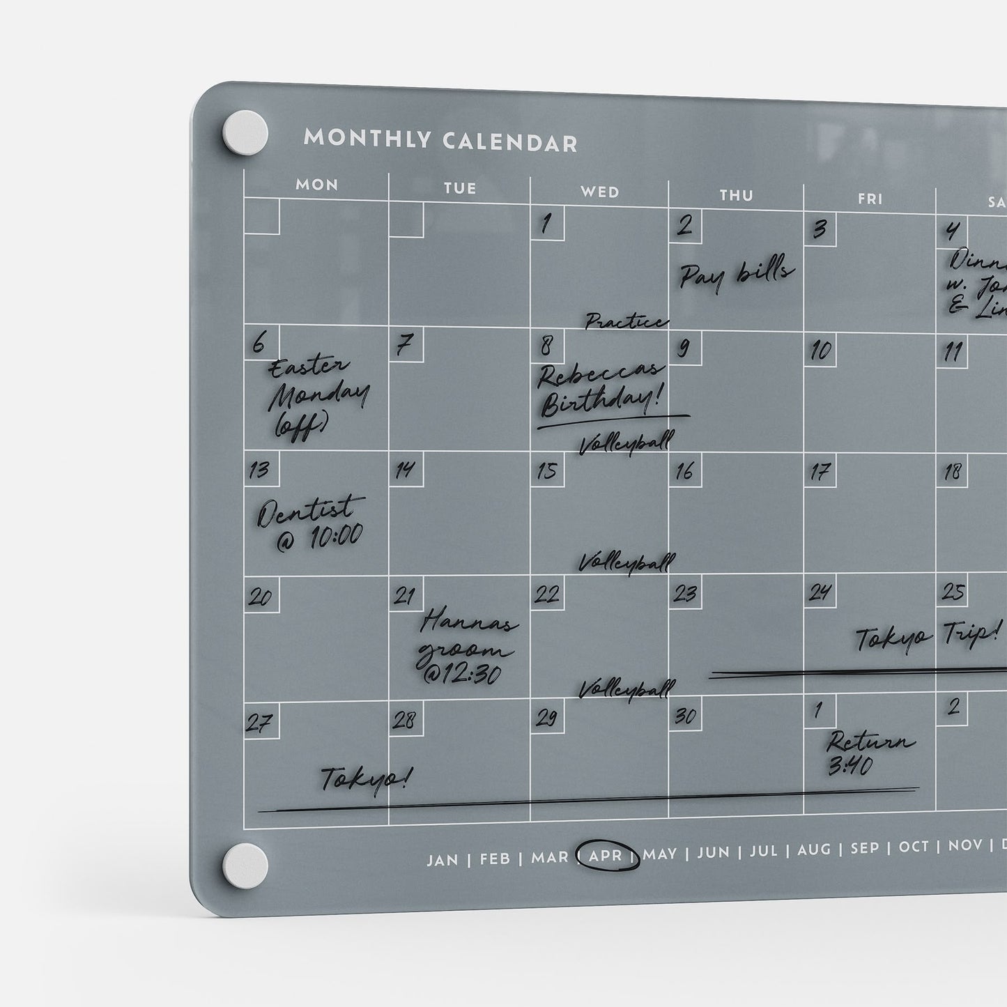 The Monthly Calendar 118, a gray compact organizer, helps families track handwritten April events like Easter, dentist visits, volleyball games, practices, bill deadlines, a Tokyo trip, and Rebecca's birthday.