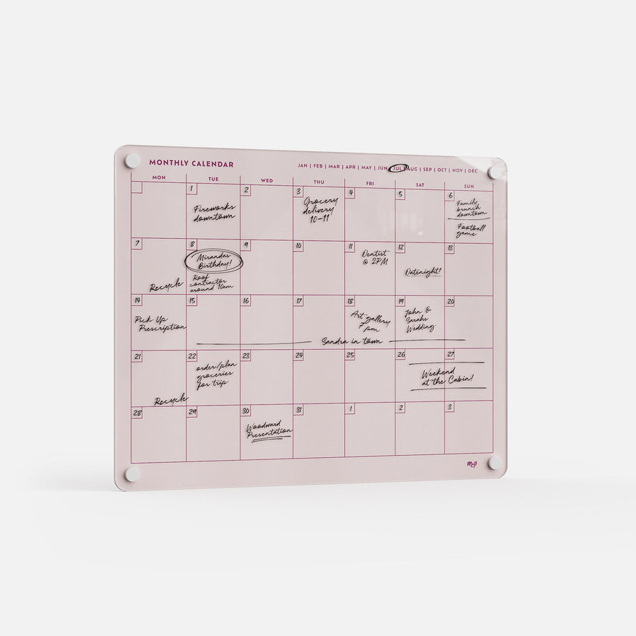 The Monthly Calendar 1411 is a pink dry-erase planner with handwritten notes and events. Ideal for family scheduling, it mounts on a white wall with four round magnets at the corners for easy planning and organization.