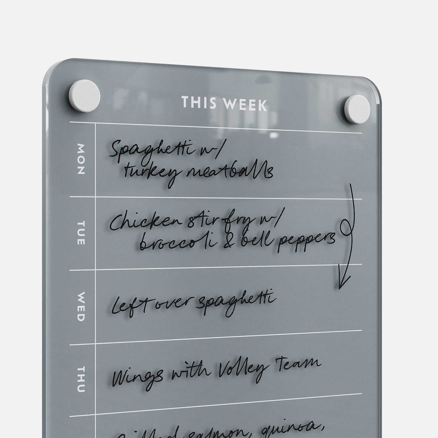 The This Week 69 glass organizer displays a weekly meal plan: Monday—Spaghetti with turkey meatballs; Tuesday—Chicken stir fry with broccoli and bell peppers; Wednesday—Leftover spaghetti; Thursday—Wings with volleyball team.
