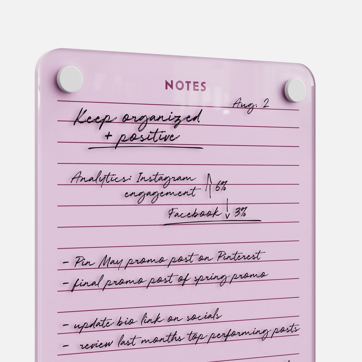 The Lined Notes 69 pink glass board labeled NOTES neatly displays handwritten lists—Instagram analytics (↑6%), Facebook stats (↓3%), promo post plans, and reminders to update the bio link and check top-performing posts.