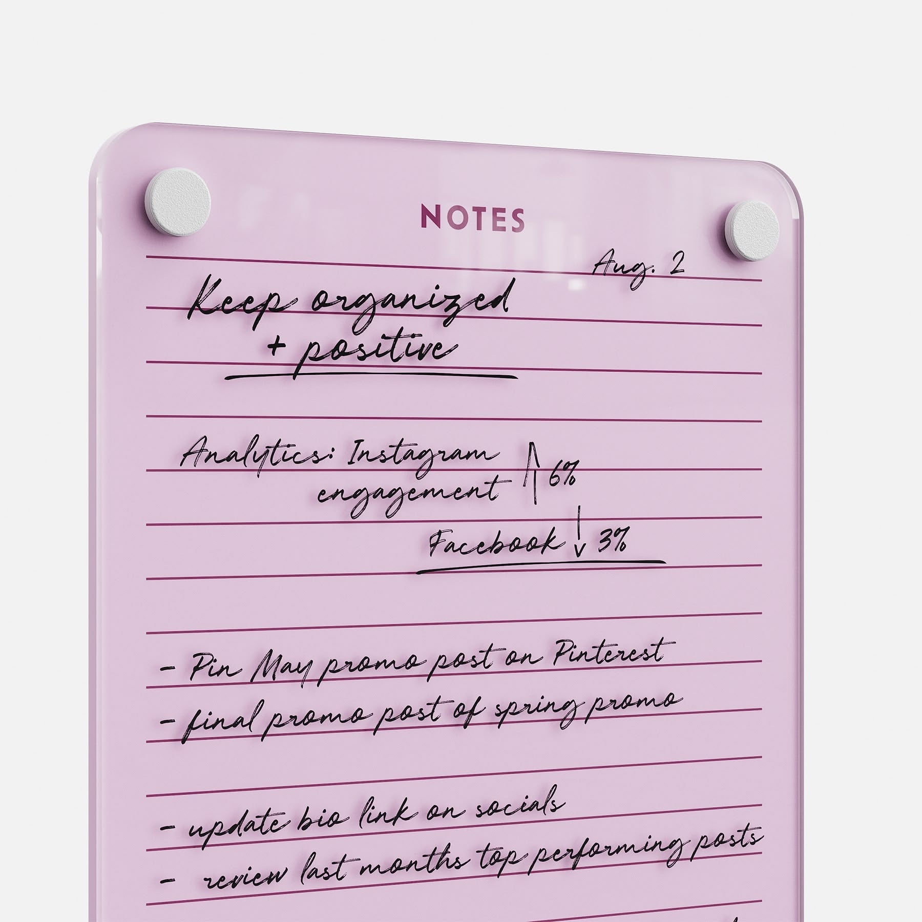 The Lined Notes 69 pink glass board labeled NOTES neatly displays handwritten lists—Instagram analytics (↑6%), Facebook stats (↓3%), promo post plans, and reminders to update the bio link and check top-performing posts.