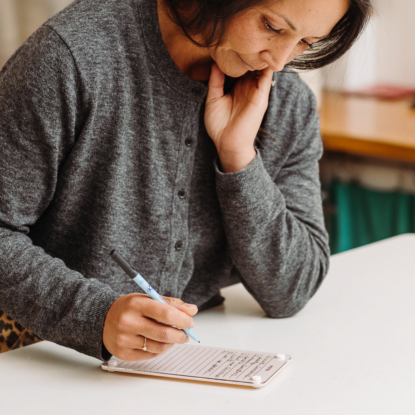 A person in a gray cardigan thoughtfully writes meeting notes with a blue pen in the Monkey and Pebbles Lined Notes 59 notebook.