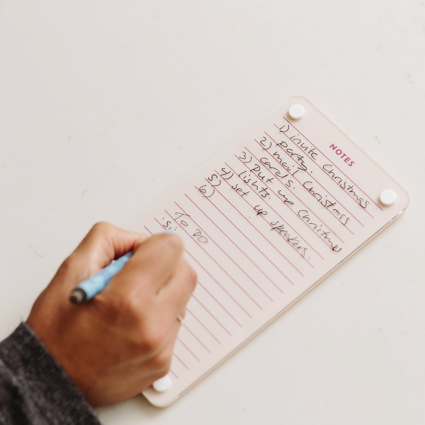 Someone writes meeting notes with a blue pen on a small Monkey and Pebbles Lined Notes 59 notebook labeled NOTES. The list has five items, some crossed out, and "TO DO" is written at the bottom.