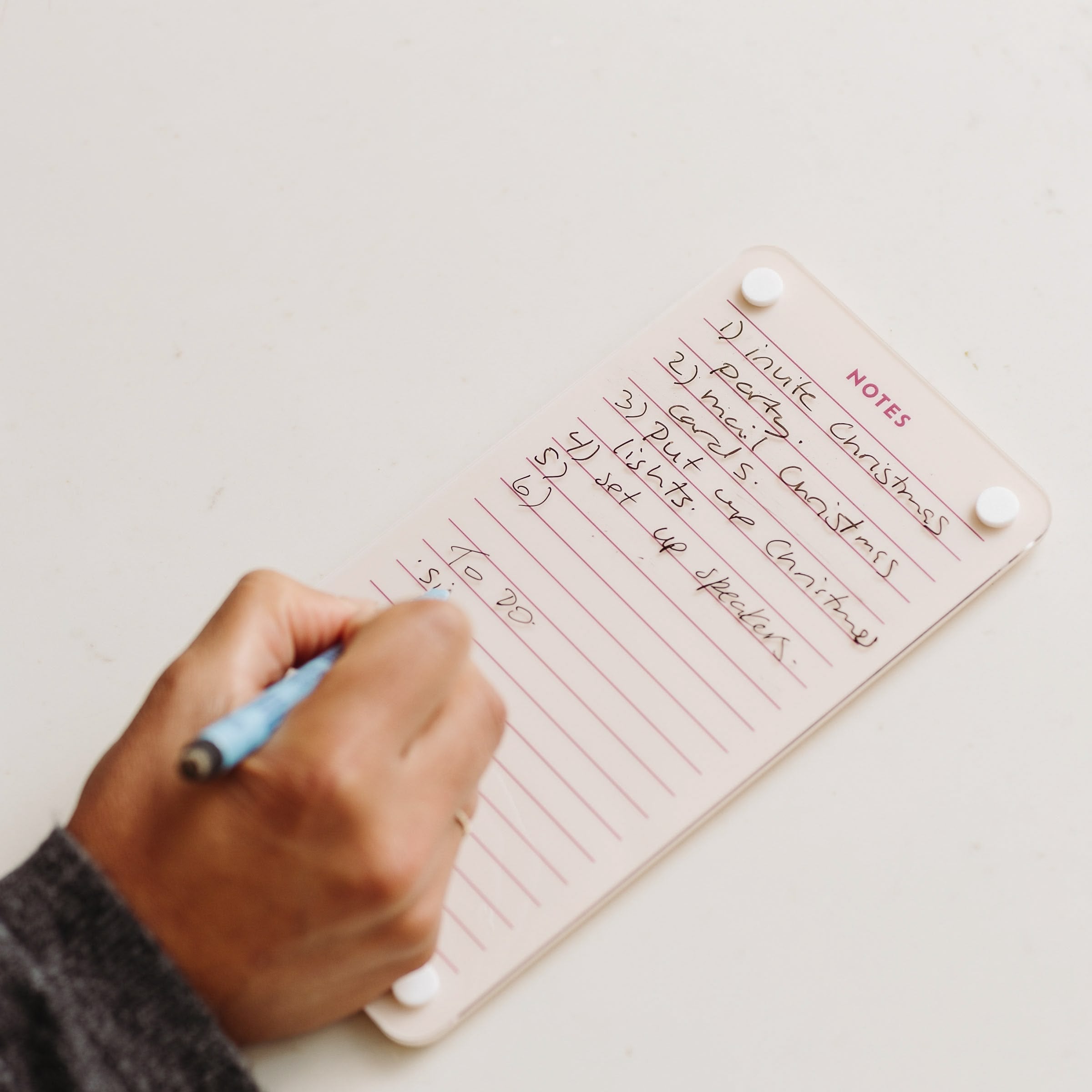 Someone writes meeting notes with a blue pen on a small Monkey and Pebbles Lined Notes 59 notebook labeled NOTES. The list has five items, some crossed out, and "TO DO" is written at the bottom.