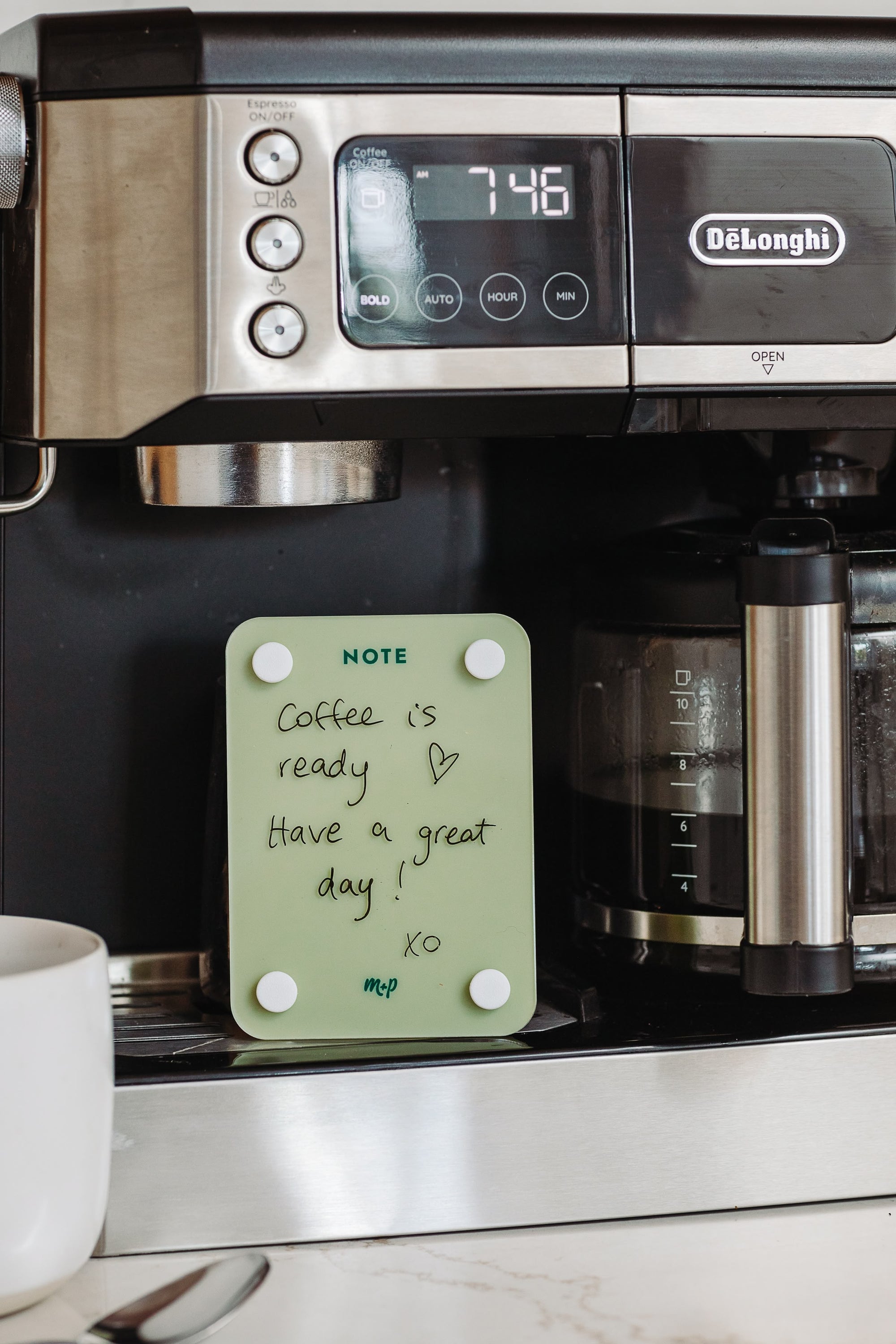 Matcha green magnetic note board on a coffee machine with a handwritten message that reads Coffee is ready, have a great day