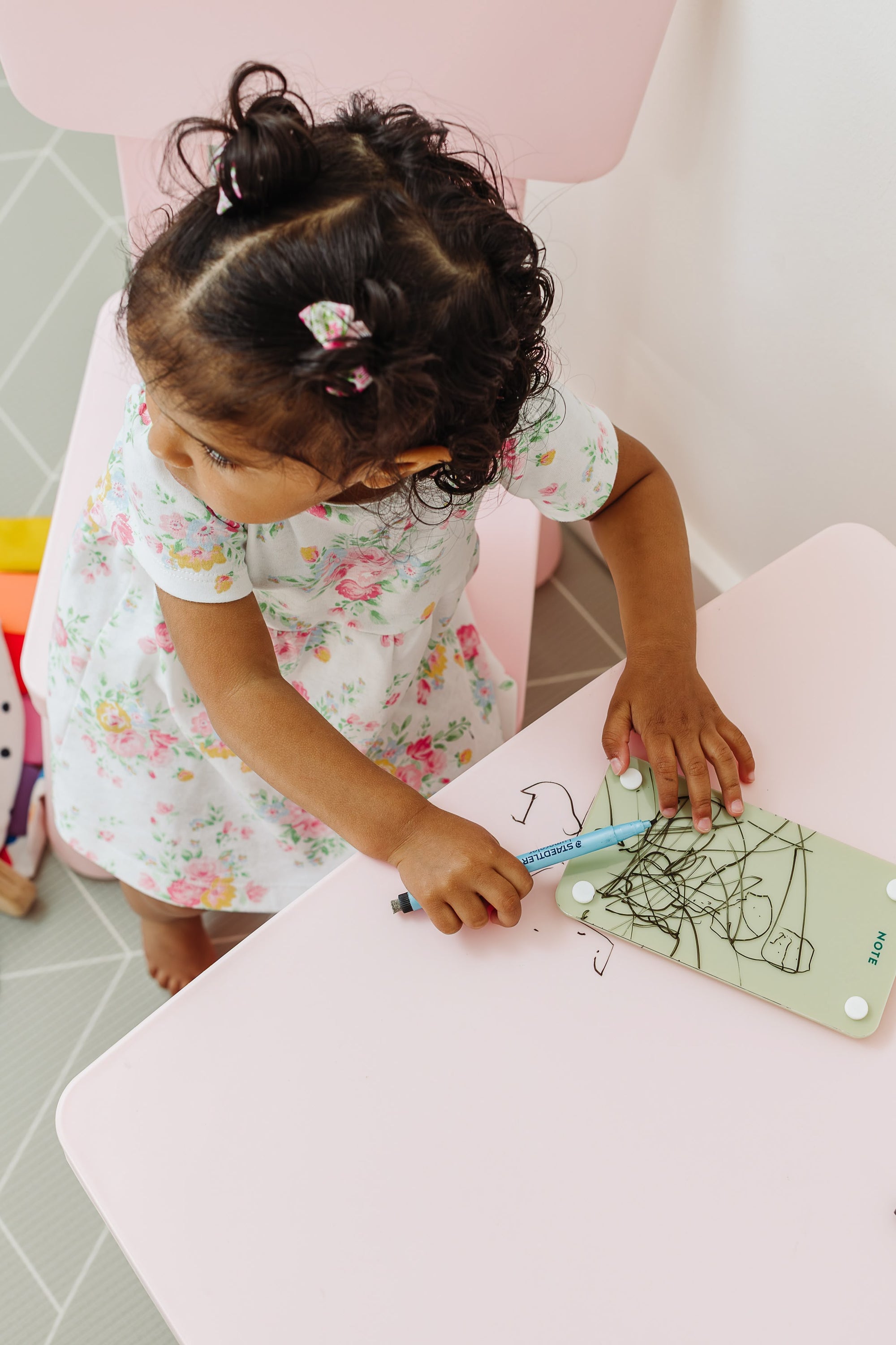 Toddler drawing on a Matcha green magnetic dry erase note board at a pink play table