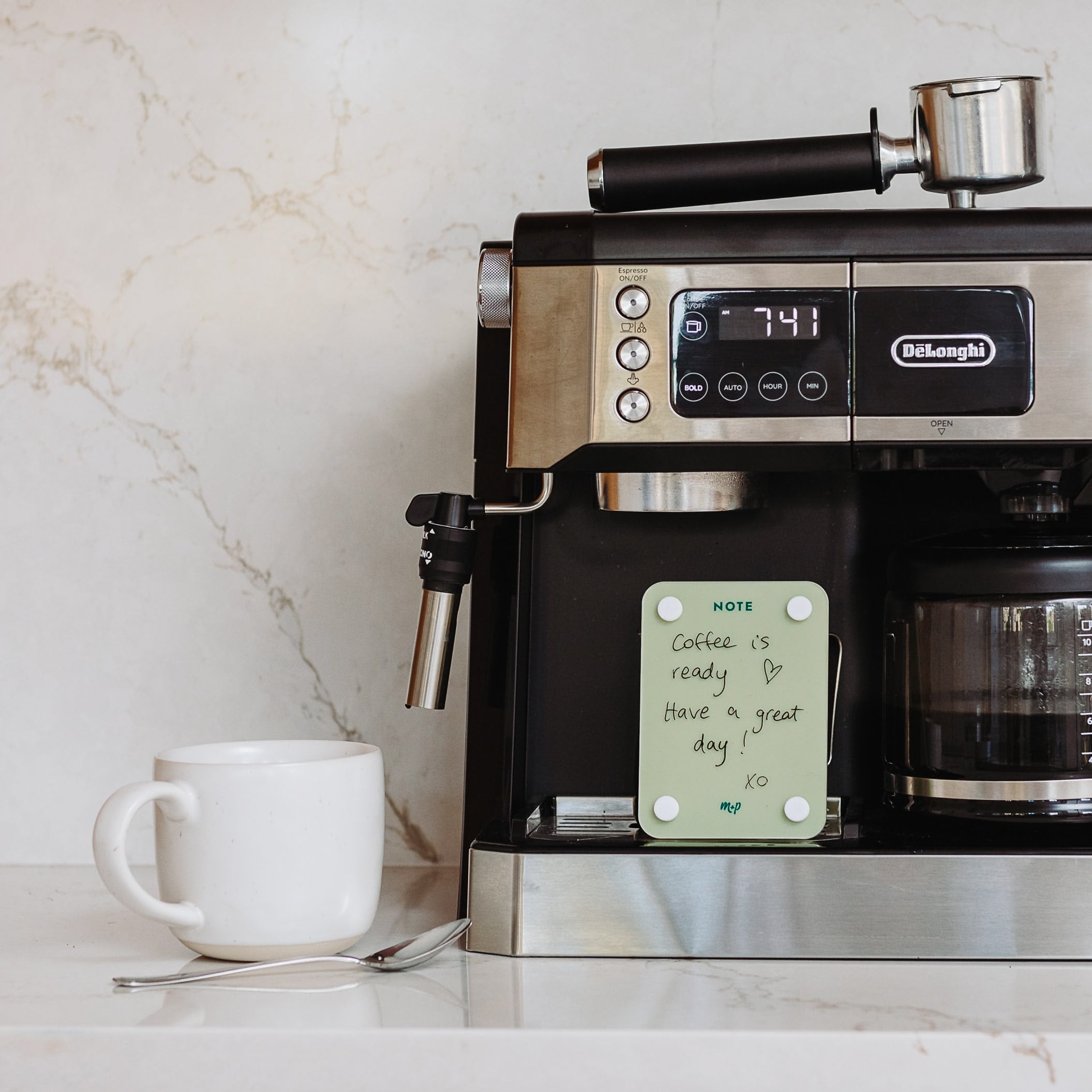 A coffee maker sits on the counter beside a mug and spoon. A Monkey and Pebbles Little Note 35 sticky note on the machine reads, Coffee is ready. Have a great day! XO.