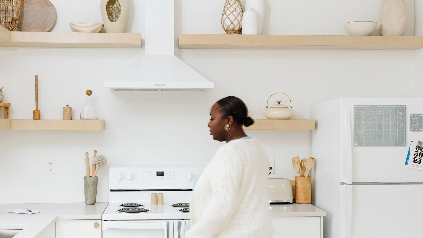 Woman standing in a modern minimalist kitchen with a Monkey and Pebbles magnetic planner board displayed on the fridge