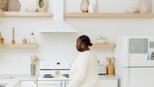 Woman standing in a modern minimalist kitchen with a Monkey and Pebbles magnetic planner board displayed on the fridge