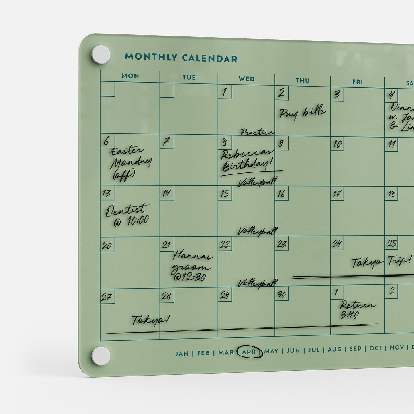 The Monthly Calendar 118 is a glass planner board for April, featuring handwritten events like Easter Monday, Dentist @ 10:00, Volleyball, Tokyo Trip!, and bill reminders—ideal as a compact calendar or family organizer for busy schedules.