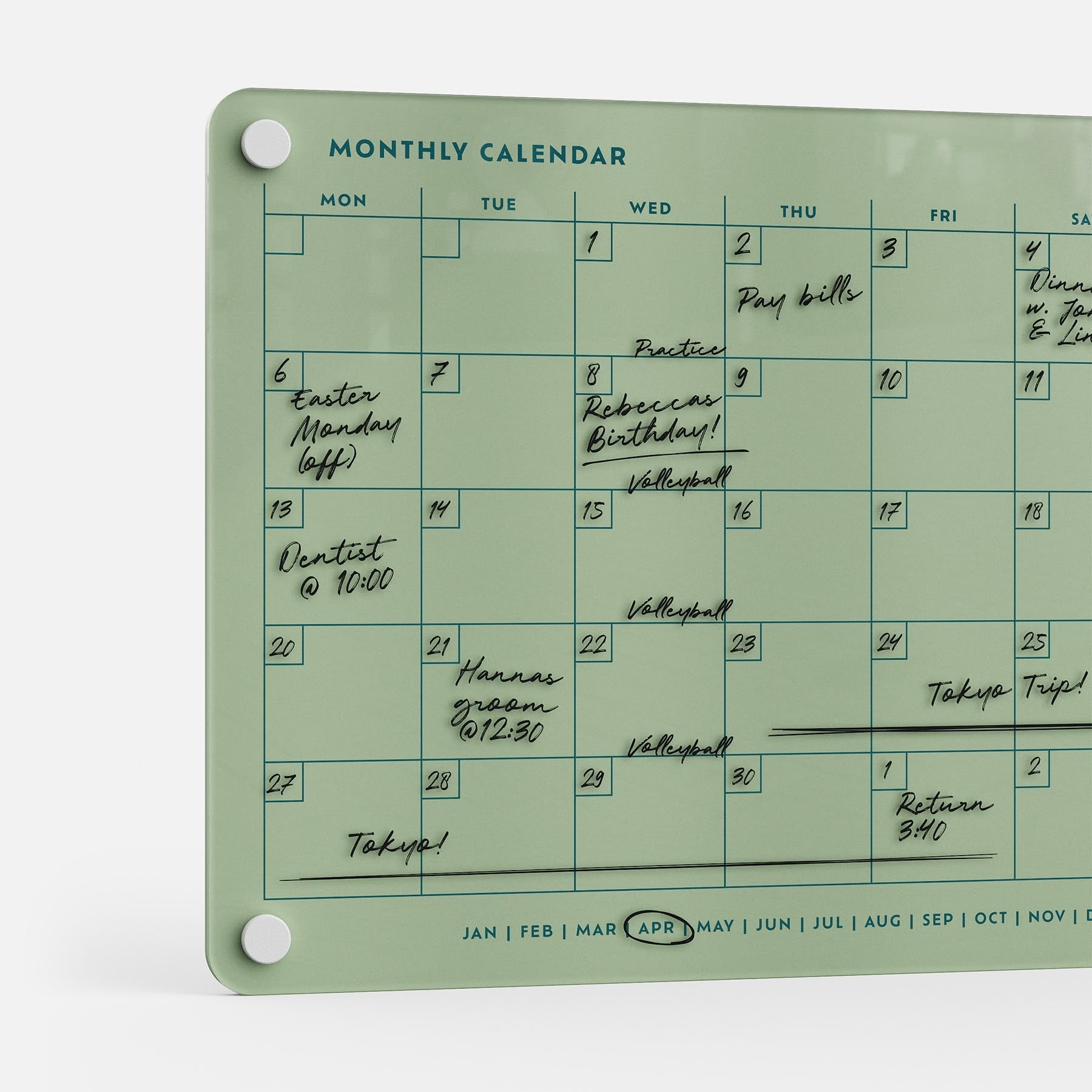 The Monthly Calendar 118 is a glass planner board for April, featuring handwritten events like Easter Monday, Dentist @ 10:00, Volleyball, Tokyo Trip!, and bill reminders—ideal as a compact calendar or family organizer for busy schedules.