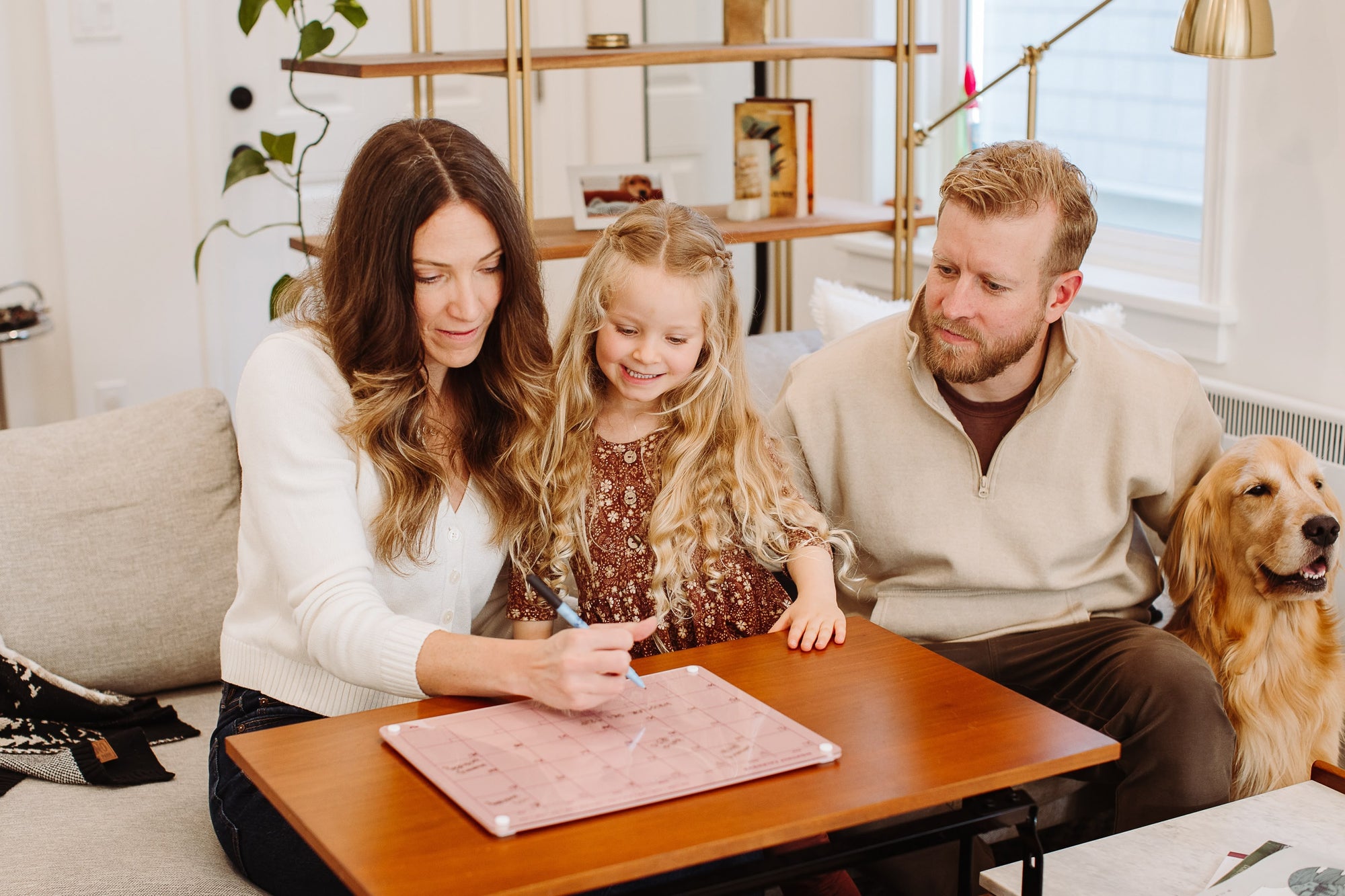 Family of three and a golden retriever planning the month on a Plum magnetic dry erase calendar on a living room coffee table