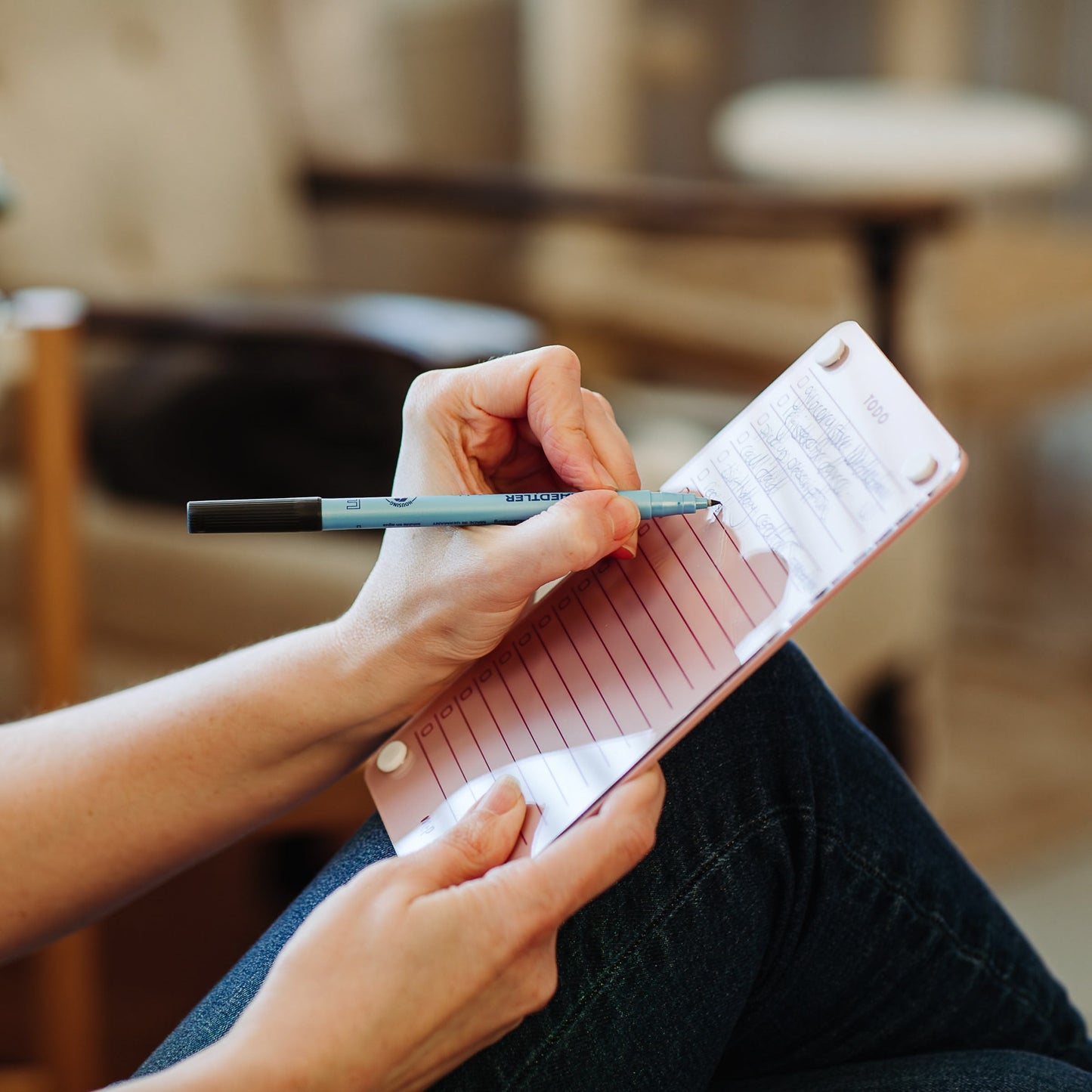 A person sits cross-legged in a cozy indoor setting, writing on the lined paper of the Monkey and Pebbles Todo List 59 task organizer notepad.