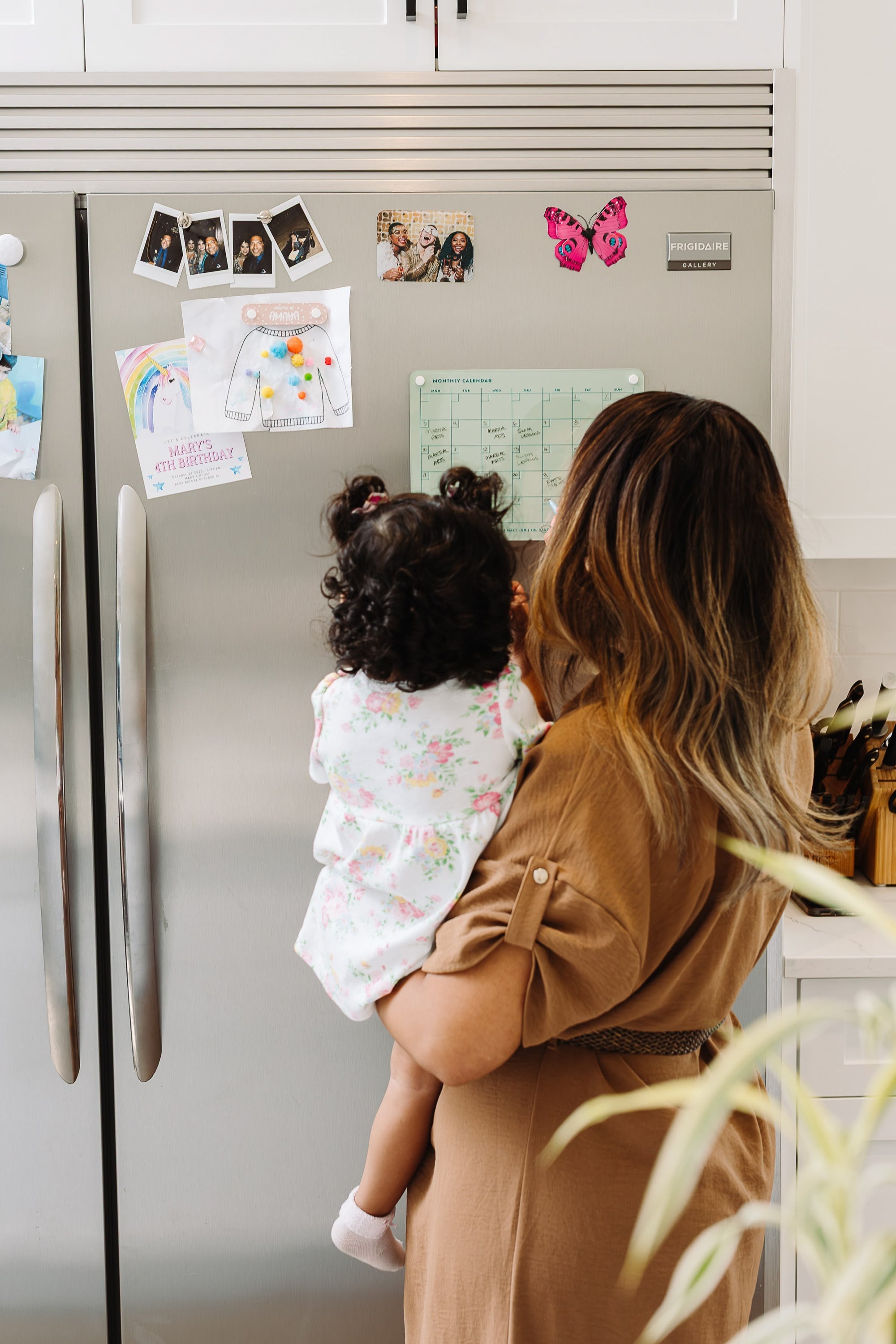 Woman holding a toddler in front of a Seafoam magnetic dry erase monthly calendar on a kitchen fridge