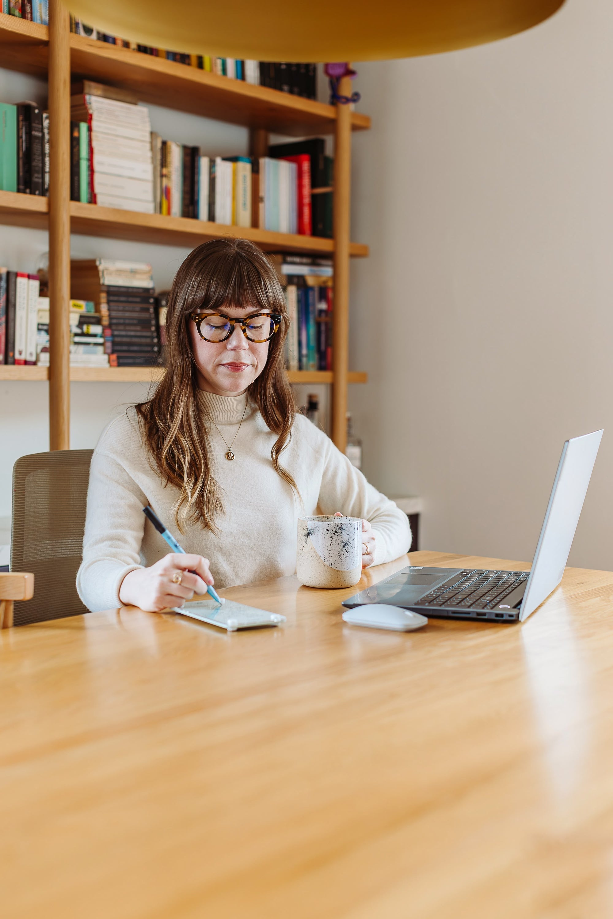 Woman writing on a Seafoam magnetic dry erase note board at a home office desk with a laptop and coffee