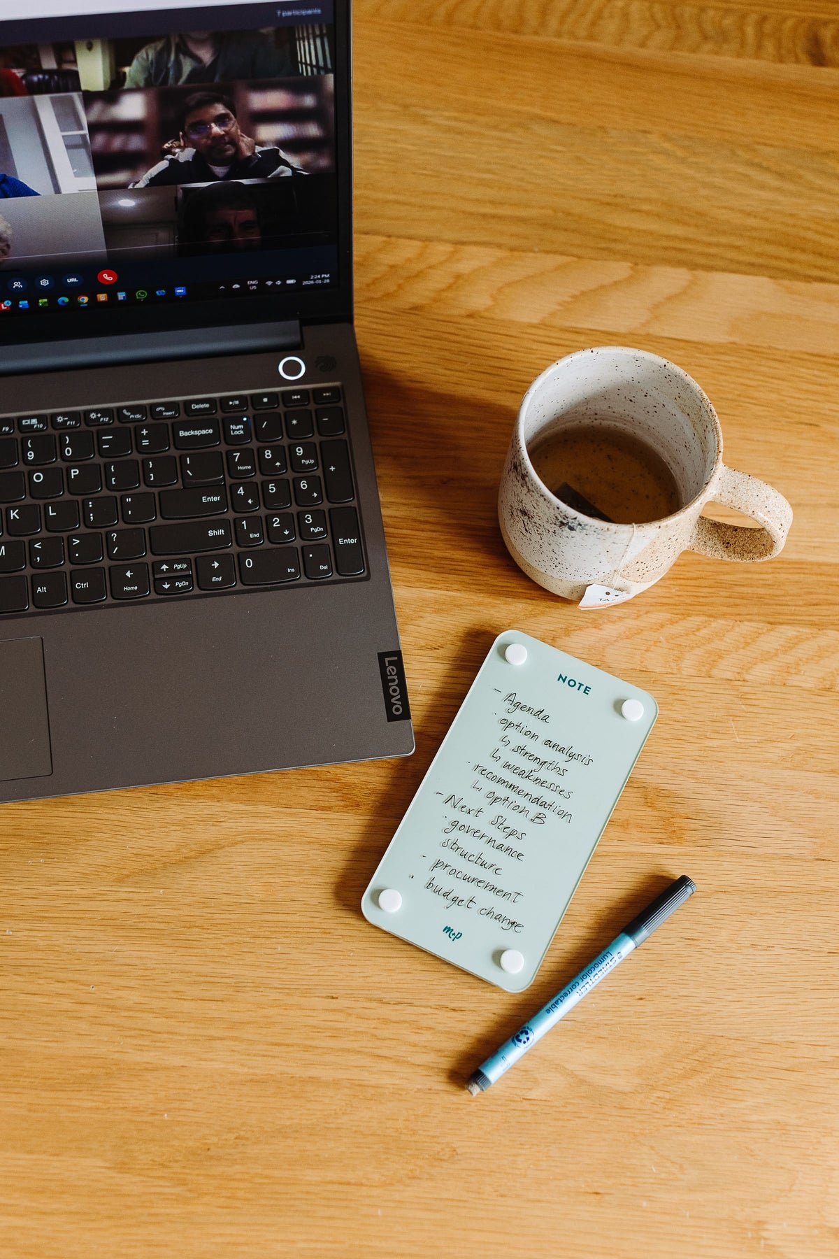 Seafoam magnetic dry erase note board with handwritten meeting notes beside a laptop on a video call