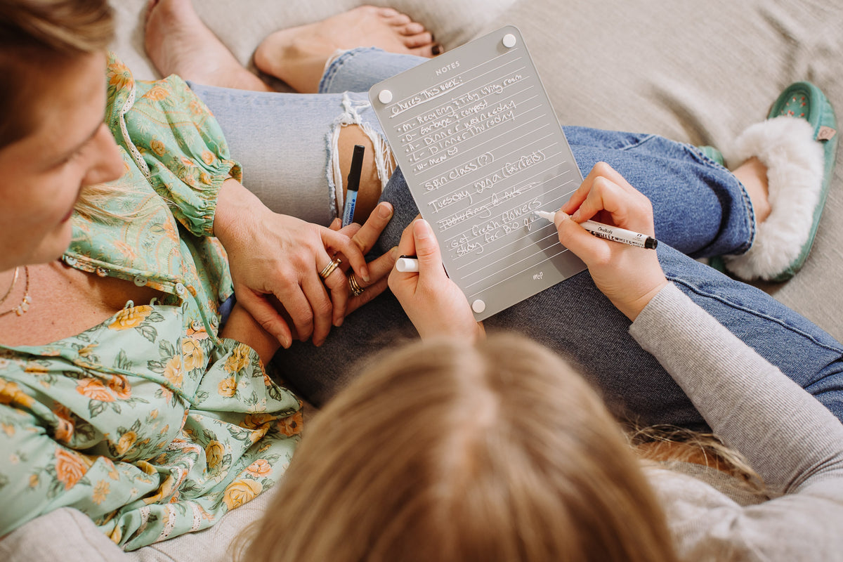 Overhead view of a family chore list for the week written on a Slate grey magnetic dry erase lined notes board