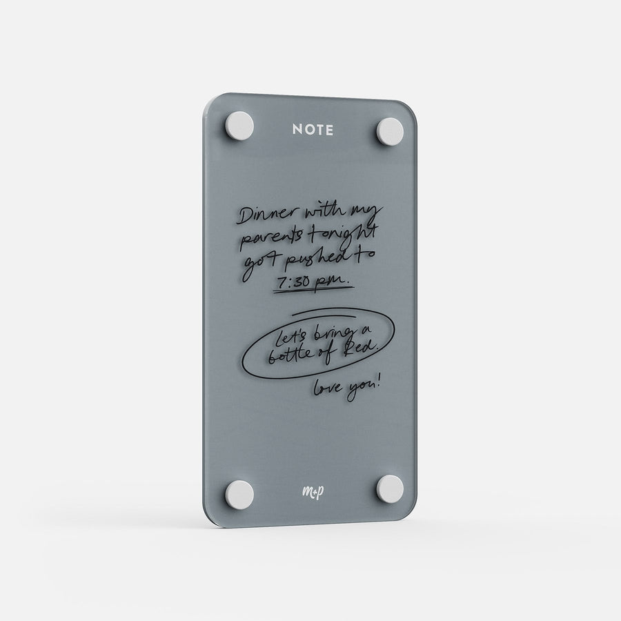 The Tall Note 47 glass message board displays handwritten reminders—like “Dinner with my parents tonight got pushed to 7:30 p.m.” and “Let’s bring a bottle of red! love you!”—and is labeled “NOTE” at the top, held by round magnets.