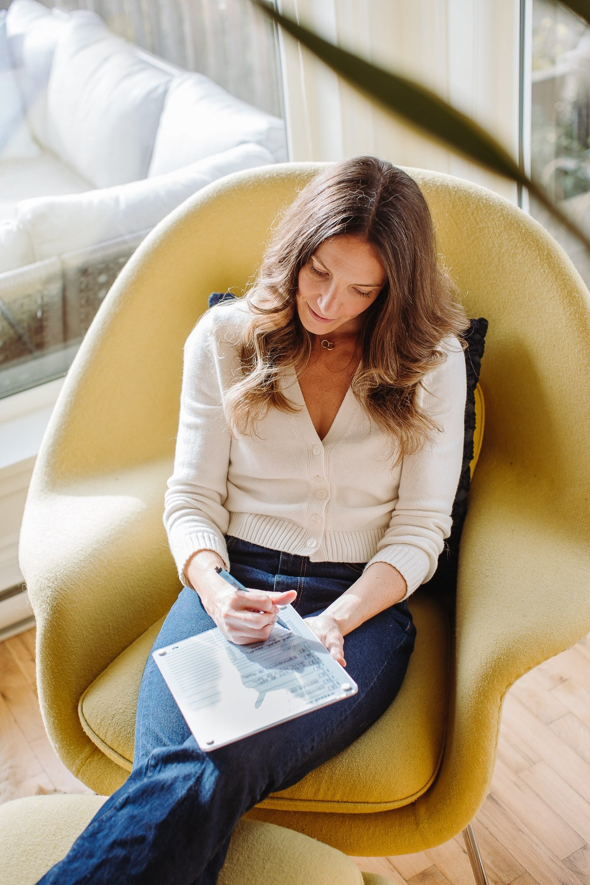 Woman planning her week on a Vista magnetic dry erase weekly planner board in a sunlit armchair