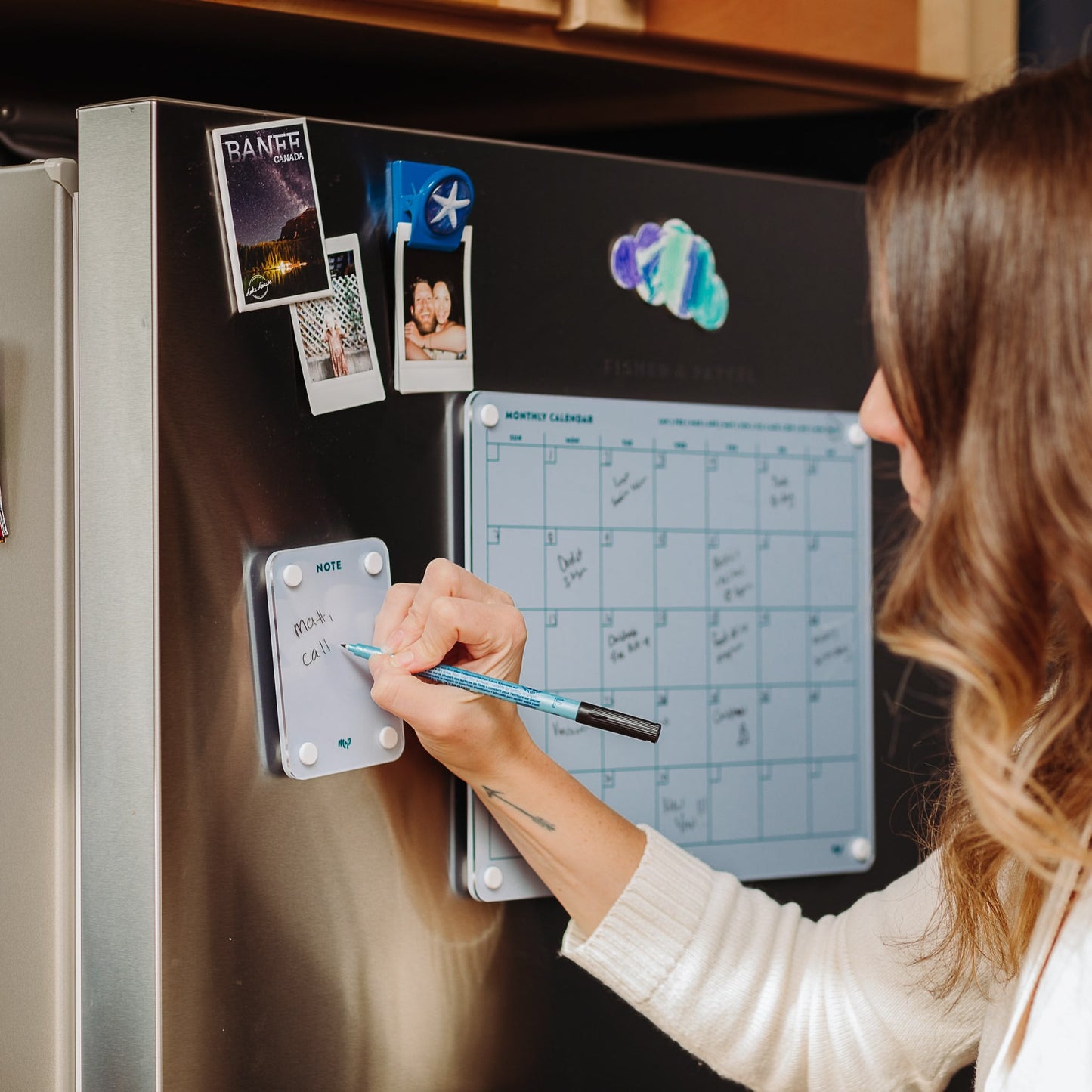 A woman uses the Monkey and Pebbles Everyday Home Bundle—magnetic dry-erase boards and calendars on her fridge—for notes, photos, home organization, and planning shopping lists.