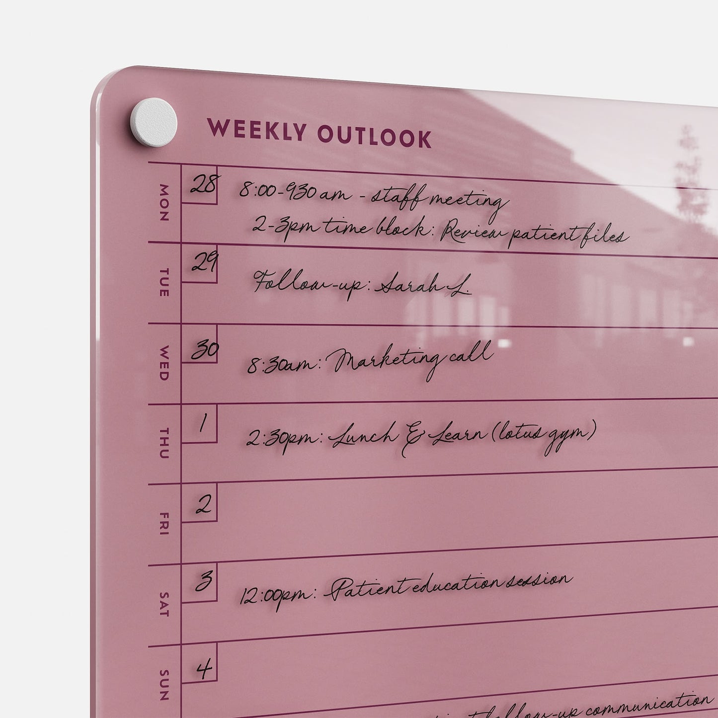 The Weekly Outlook 811, a pink dry-erase wall planner, organizes tasks and appointments such as meetings, Lunch & Learn, and patient education sessions, with days of the week listed on the left for easy weekly planning.